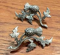 Two pewter thistle motif earrings front view on wood surface