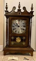Front view of wood clock showing dial, pendulum window, finials and columns