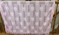 Pink crocheted lace tablecloth with fringed edge draped over railing
