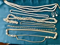 All jewellery pieces laid out on teal fabric, showing pearls, gold-tone chains, earrings and bracelet