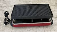 Raclette grill assembled with cord attached, pans visible