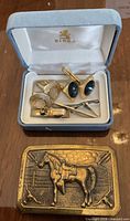 Open Birks case with two cufflink pairs and two tie clips, belt buckle placed below