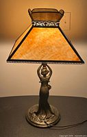 Lamp lit, showing bronze-finish female figure base and caramel slag glass shade