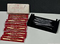 Lot overview showing red-sleeved gold bands, silver-tone stretch bands on black tray, and Shuttlecock retail box