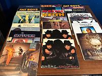Overview of 26 vinyl record sleeves on table including Run-D.M.C., Kool & the Gang, Coolio and others