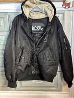 Front view of black Projek Raw Dark Black hooded bomber jacket on hanger