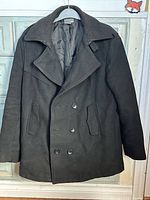 Front of black double-breasted pea coat on hanger