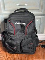 Front view of black Husky tool backpack showing logo, red piping and multiple pockets