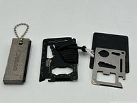 Three survival tools laid out: Coghlans block, Yukon Gear card, stainless card with sleeve