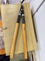 Full view of loppers showing 27" length, wood handles, black metal neck, curved blade