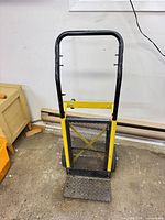 Front view of black and yellow steel hand truck, mesh panel, diamond plate toe plate