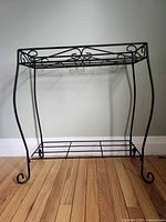 Full view of black metal plant stand with scroll design and two shelves