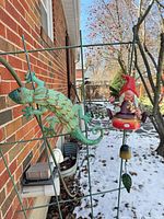 Lizard sculpture and gnome bell hanging on metal trellis outdoors in winter setting