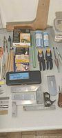 Overview of assorted drafting, bookbinding and hand tools including wooden T-square, compasses, boxes of tape, clamps, pencils and measuring tools