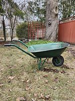 Side view of green metal wheelbarrow on lawn showing frame, wheel, handles