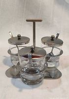 Front view showing three glass jars in stainless stand with lids and spoons
