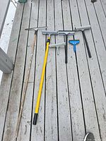 five squeegees and two extension poles laid on decking