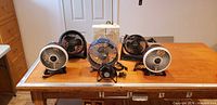 Group of Duracraft box fan and five desk fans on table