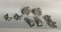 Seven silver-tone rhinestone jewelry pieces laid out