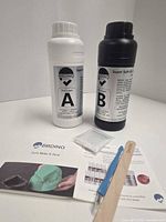 Full kit showing Part A and Part B bottles, mixing stick, blue spreader, booklet, small clear bag