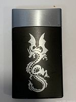 Front view of lighter showing black body, silver dragon graphic, chrome top