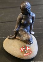 Overall view of bronze-tone seated woman figurine on stone base with Danish flags and text