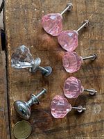 five pink faceted glass pulls, one clear faceted pull, one chrome pull displayed on wood surface