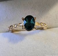 Gold-tone ring with dark green oval stone and clear accents displayed in box
