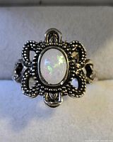 Front view of ring showing oval opalescent cabochon and ornate silver-tone filigree setting