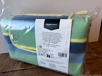 Front of packaged folded Amazon Basics picnic blanket with label showing brand and folded tote form