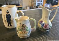 Three porcelain items: London officer mug, scenic creamer, floral vase on table