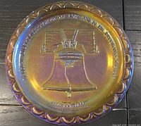 Front view of iridescent marigold carnival glass plate with Liberty Bell design