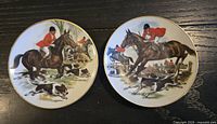 Front view of both decorative plates showing fox-hunting scenes and gold rims