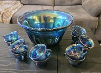 Large iridescent punch bowl with surrounding cups displayed on table