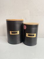 Front view of both black metal canisters with bamboo lids and gold label holders
