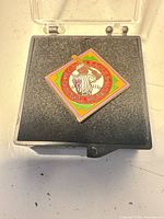 Diamond-shaped enamel pin on foam insert in open plastic case