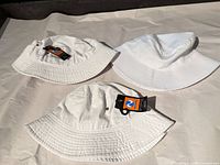 Three white bucket hats, two with tags visible