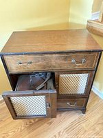Front view of wooden console phonograph cabinet showing drawer, mesh door and interior turntable