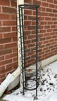 Full view of cylindrical black iron trellis against brick wall