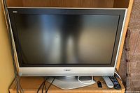 Front view of Panasonic TV on stand with two remotes and cables