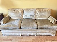 Front view of gold colour three-seat sofa showing overall design, cushions, skirted base