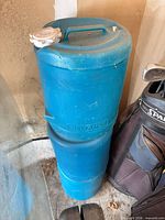 Two stacked blue plastic cylindrical water jugs beside golf bag