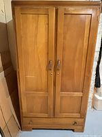 Front view of light brown wood wardrobe with two paneled doors and bottom drawer