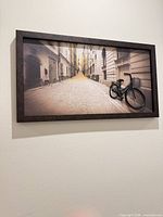 Full view of framed wall art showing street scene and 3-D bicycle