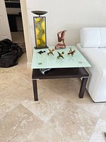 End table showing glass top, wood base, lamp, sculpture and metal jacks