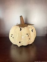 Front angled view showing ceramic pumpkin form, cutouts, metal stem