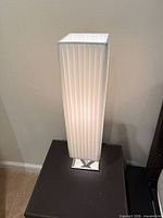 Lamp illuminated showing pleated white shade and chrome base