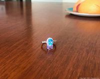 Full view of ring on stand showing blue topaz center and halo