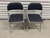 Front view of two grey metal folding chairs with blue padded seats and backs