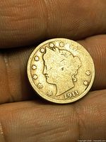 Obverse view of 1911 Liberty Head V nickel held between fingers